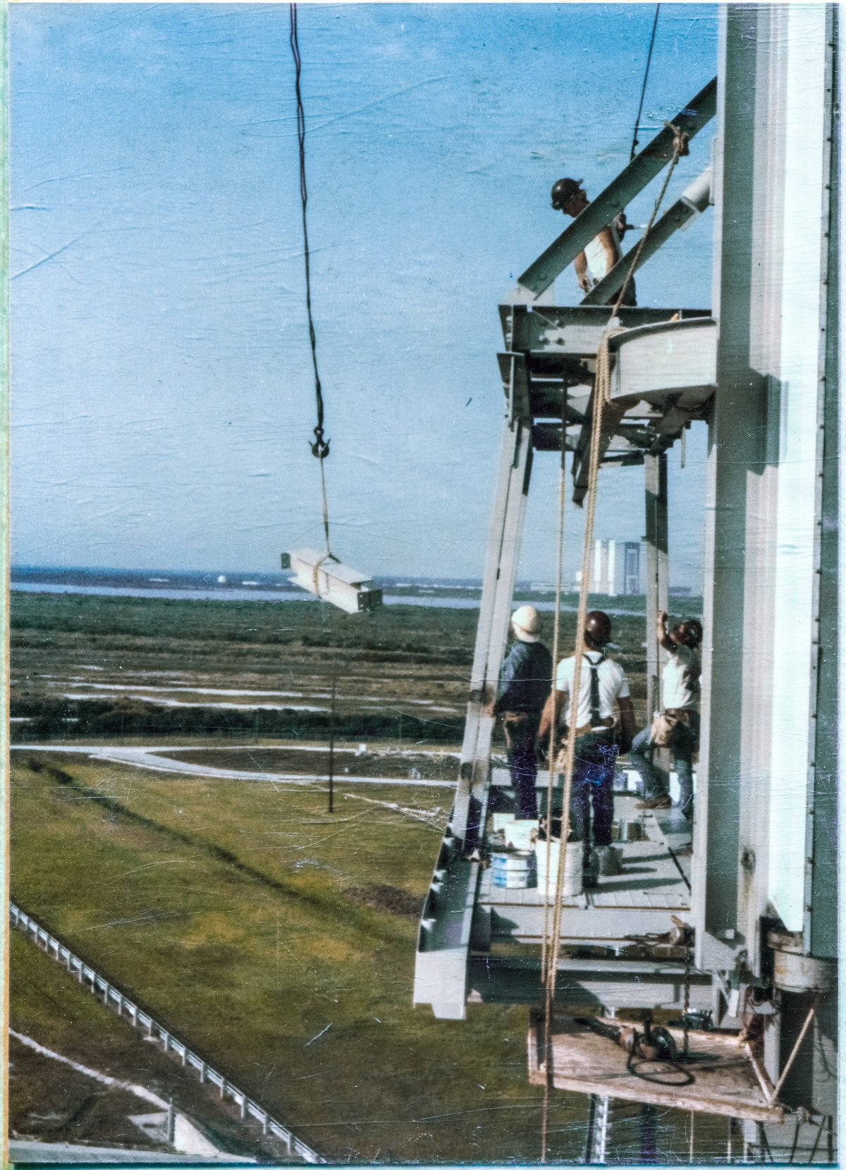 Image 058. Union Ironworkers from Local 808 working for Ivey's Steel Erectors at Space Shuttle Launch Complex 39-B, Kennedy Space Center, Florida, prepare to receive an inbound steel beam, which will be attached to the reworked PBK & Contingency Platform which they are standing on, and above, out in front of the face of the  Rotating Service Structure, an unimpeded 80 foot free drop above the concrete surface of the Pad Deck, beneath them. There is a story with the rework of this platforming, and it is not a pleasant one. Construction work, and Operations work too, in areas like this, is never to be taken for granted, and you must never let your guard down, lest you become an unwilling part of the “contingency” yourself. Photo by James MacLaren.